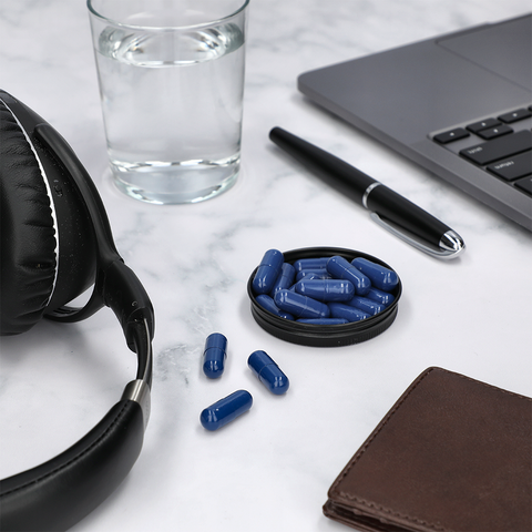 Hung Daily – Blue Pills on Marble Tabletop with Technology and Water Glass